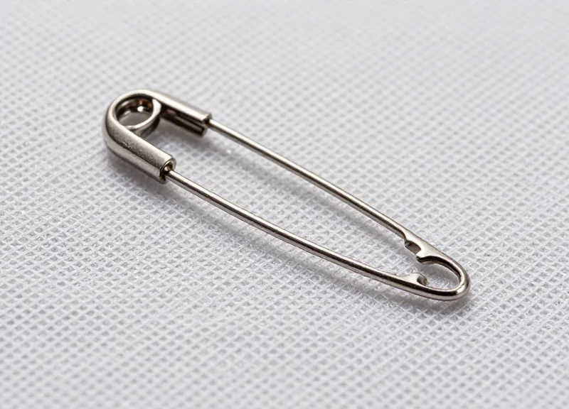 Macro photography of a thin, sharp stainless steel security pin piercing high-performance athletic fabric.