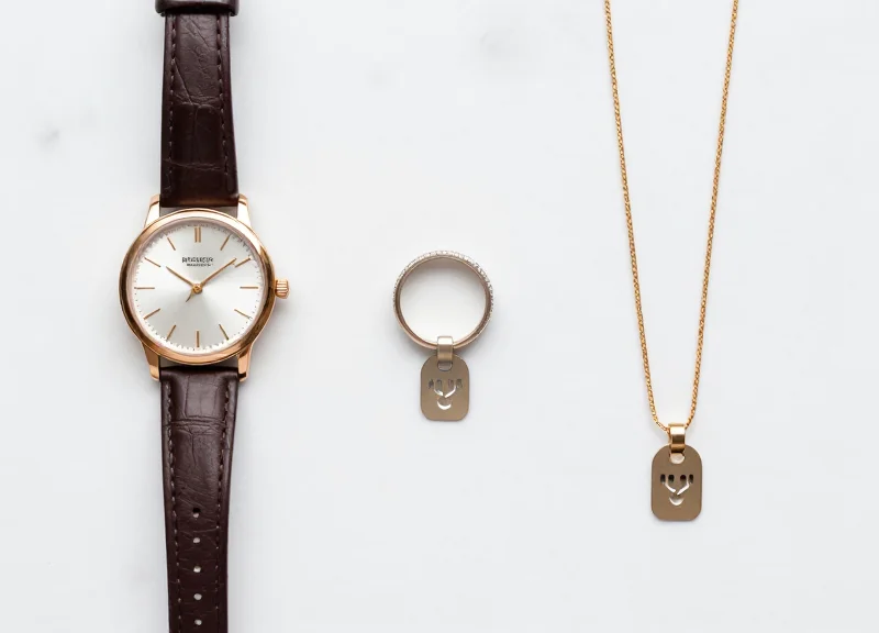 Top-down view of a watch, ring, and necklace neatly arranged with tiny security tags on a marble surface.