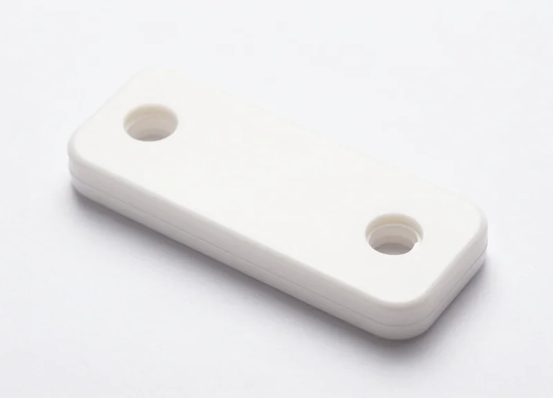A close-up of a standard white plastic EAS security tag used in retail pharmacies.