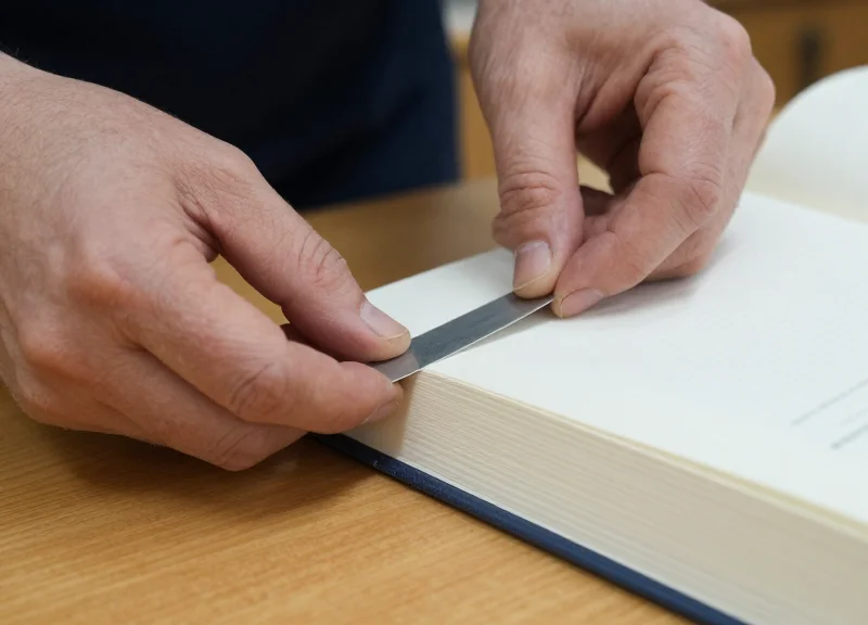 Close-up of a librarian's hands applying a security strip into the spine of an old hardcover book