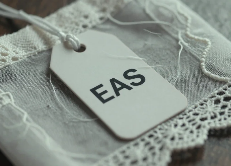 Close-up of a heavy security tag pulling on delicate silk lace, showing visible fabric tension.
