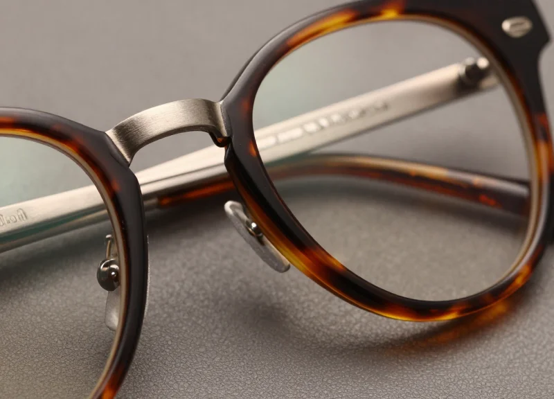 Macro photography of polished tortoiseshell acetate and brushed titanium eyewear frame materials.
