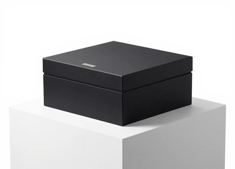 A minimalist black luxury box with a discreet security label on a white pedestal