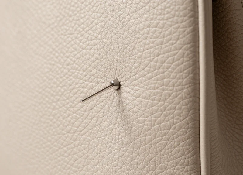 Macro photography of a luxury leather handbag surface with a delicate metallic security pin.