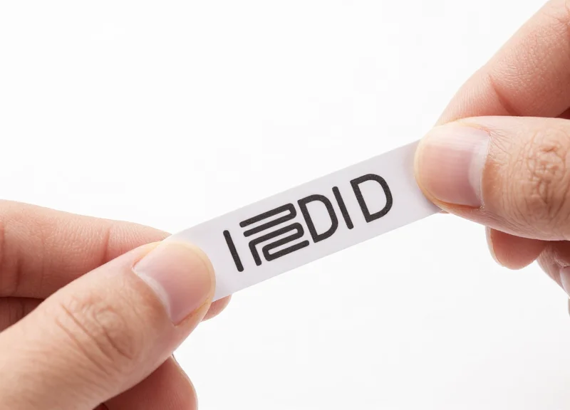 Macro photograph of a flexible RFID tag being bent, showing its thin and adaptable structure on a white background.