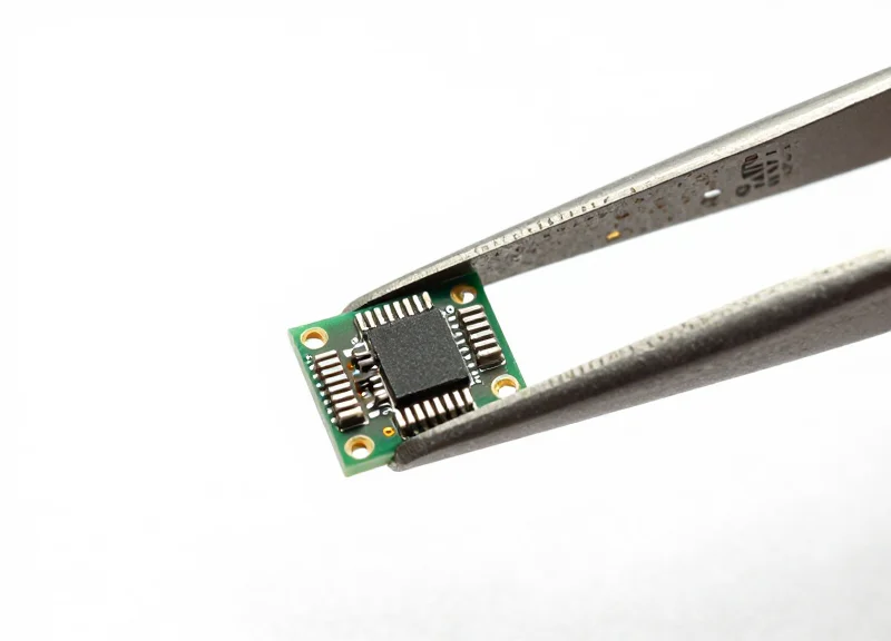 A micro-sized RFID module held by industrial tweezers to show scale and precision.